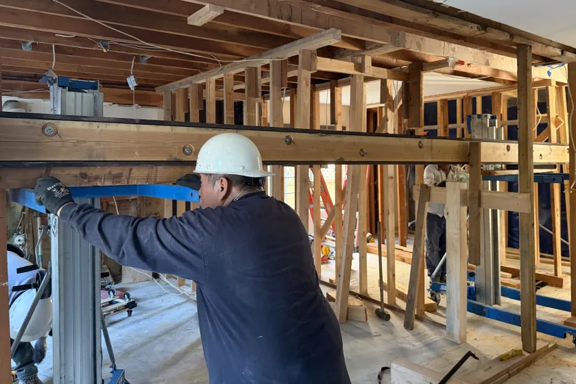 Worker in a hard hat beside wood framing and a beam during a home addition project