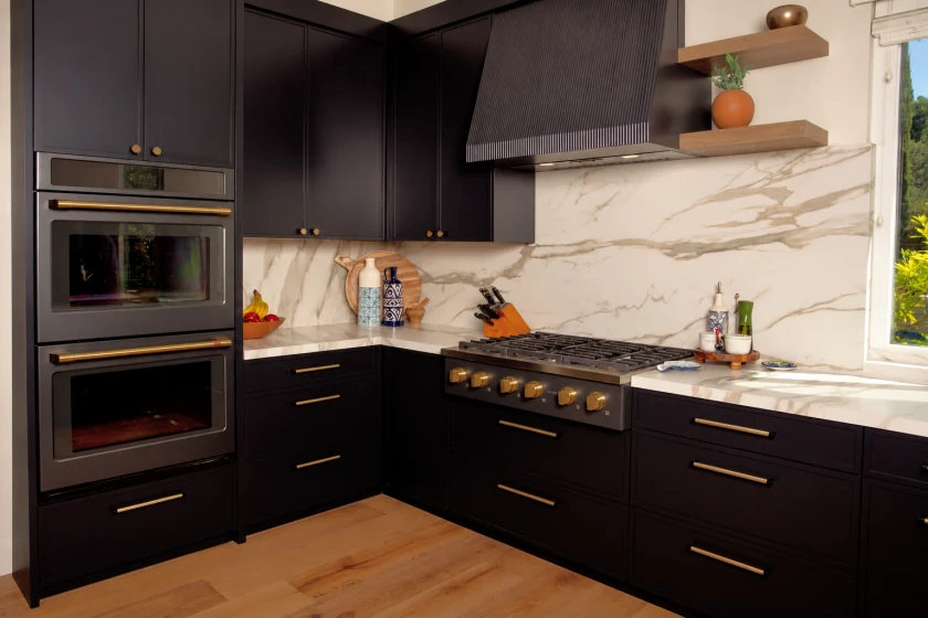 Real kitchen with dark upper cabinets, range hood, double ovens, marble-look backsplash and window